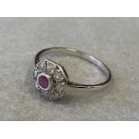 An Art Deco style white metal (probably gold) ring set with a central ruby surrounded by eight