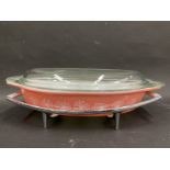 A Pyrex pink oval serving dish on a chrome plated stand.