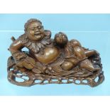 A Japanese root carving of a jolly recumbent Man and mythical beast, with inset eyes and teeth, on