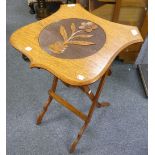 An Arts and Crafts oak folding shield-shaped Table, the top with a carved daisy, upon the folding