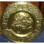 A large circular brass Charger, decorated in relief in the Dutch style with three figures around a