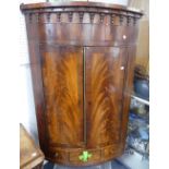 A Georgian mahogany bow-front Corner Cupboard, the moulded cornice with drop pendants above two
