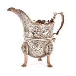 A silver cream jug, in the Irish taste, London 1899, helmet shaped, profusely chased with birds,