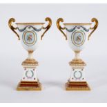 A pair of Royal Crown Derby urns on stands, each of twin-handled form with gilt borders,