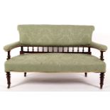 An upholstered settee with spindle turned supports and turned legs with castors,