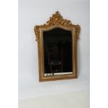 A decorative gilt framed wall mirror with shell and leaf scroll crest above an arched glass,