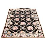 A modern needlepoint rug decorated roses among trellis on a black ground 180cm x 117cm