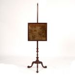 A mahogany pole screen with vase finial, the machine worked panel of a house beside a river,