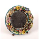 A late 19th Century Dresden circular mirror, the frame encrusted with flowers, with easel support,