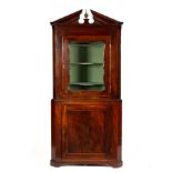 An early 19th Century mahogany corner cupboard in two sections with swan neck pediment,