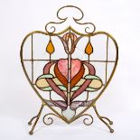 An Art Nouveau style fire screen, the brass heart shaped frame inset stained glass,