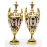 A pair of Royal Crown Derby urns, each having a lidded top, above an Imari decorated body, 12"h