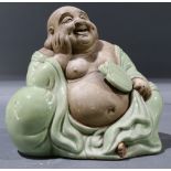 Japanese ceramic smiling Hotei, holding a fan in his left hand, wearing a pale green garment,