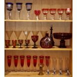 Three shelves of glassware including Bohemian style red wine glasses