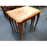 A nest of three glass topped tables with carved le