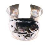 Unmarked white metal bangle of planished design with floral panel