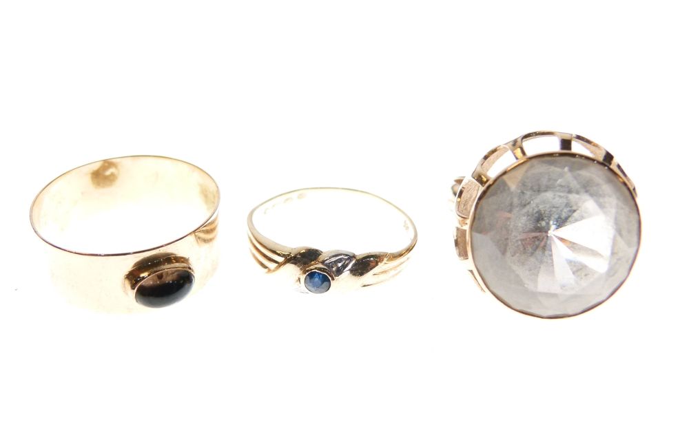 Three assorted yellow metal rings comprising a broad band ring with oval cabochon, dress ring set