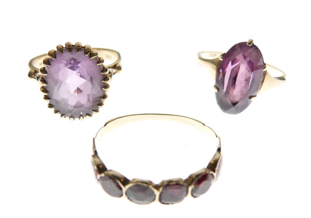 Three assorted gold and yellow metal rings, each set amethyst-coloured stones, comprising two