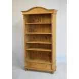 Stripped pine open bookcase with arched pediment over four adjustable shelves and base drawer on bun
