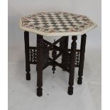 Octagonal marble and inlaid hardstone chequer board table on finely carved folding base, 62cm wide