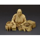 Japanese Meiji period ivory okimono, modelled as a seated male figure before a selection of wooden