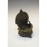 Indian or South East Asian alloy votive oil lamp, the back modelled in relief with a seated deity