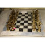 Modern chess set comprising cast metal pieces on a marble board, 40cm square