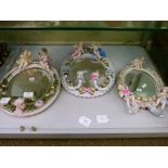 Three German porcelain oval wall mirrors, all with cherub mounts, one with sconces