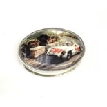 A silver oval pill box with enamel lid depicting a racing car.