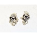 A pair of silver skull shaped earrings.