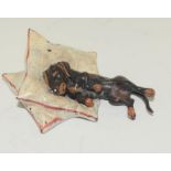 A cold painted bronze figure of a dachshund resting on a pillow.