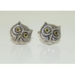 A pair of silver owl cufflinks with glass eyes.