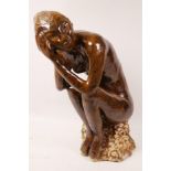 A stoneware figurine of a nude seated upon a rock (signed), 15½" high