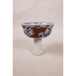 A Chinese blue and white porcelain stem cup with a ribbed stem, decorated with red carp in a lotus