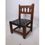 A Spanish style oak low chair with a woven leather strap seat and carved decoration, 25½" high