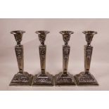 A set of four silver plate candlesticks on tapered plinths with repoussé swag and bow decoration,