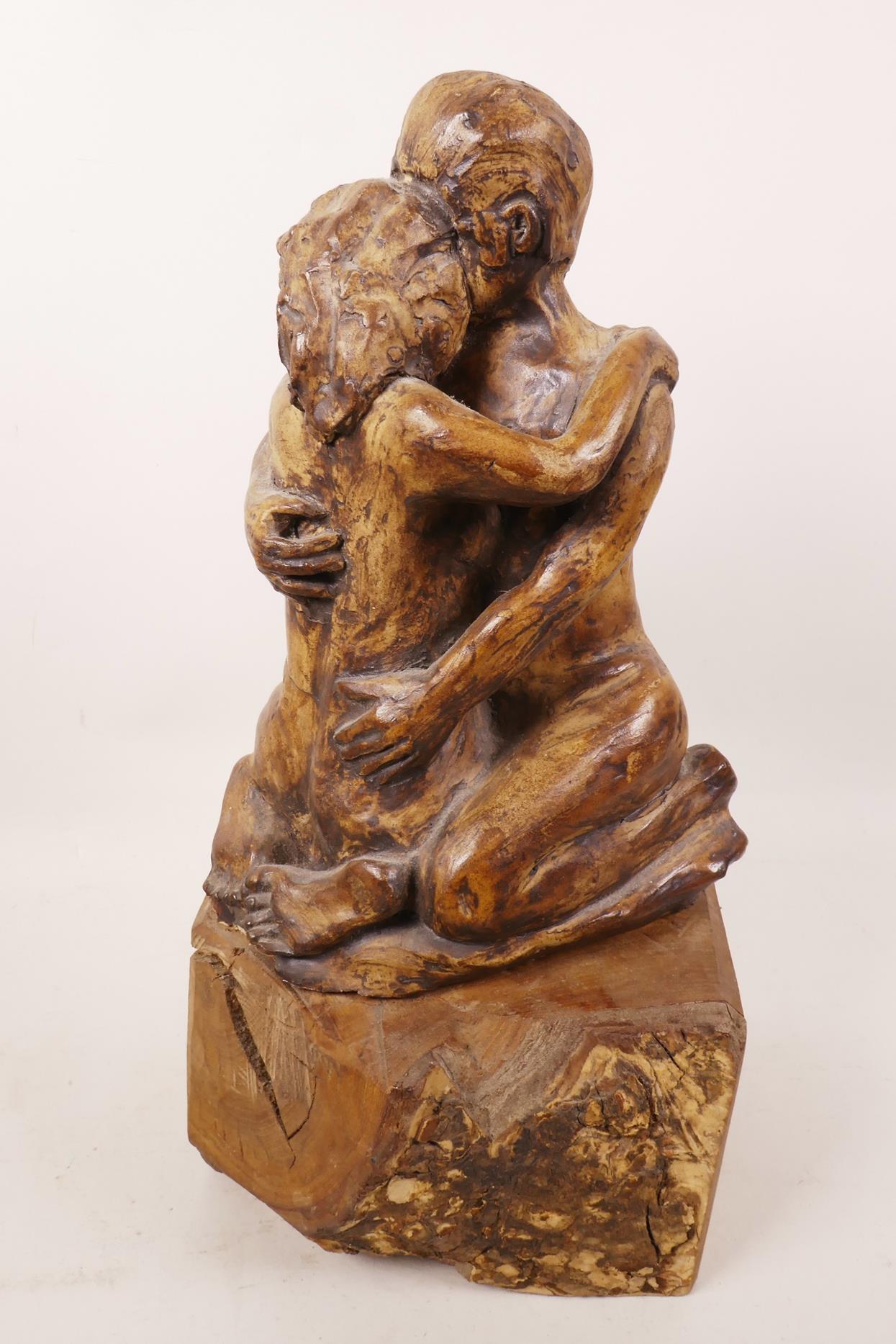 An art pottery figurine of a lovers' embrace mounted on a wooden plinth, 13½" high