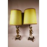 Two gold cherub table lamps, cast golden cherubs standing on black square stands, with green shades,