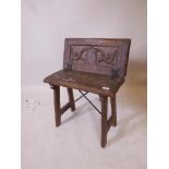 A C19th Arts and Crafts oak stool with fold over back and carved decoration, forged iron hinges