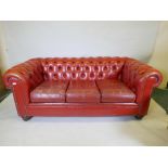 A red leather button back Chesterfield settee on turned feet, 74" long