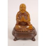 A Chinese amber soapstone carving of Lohan seated in prayer, on a hardwood stand, 3½" high
