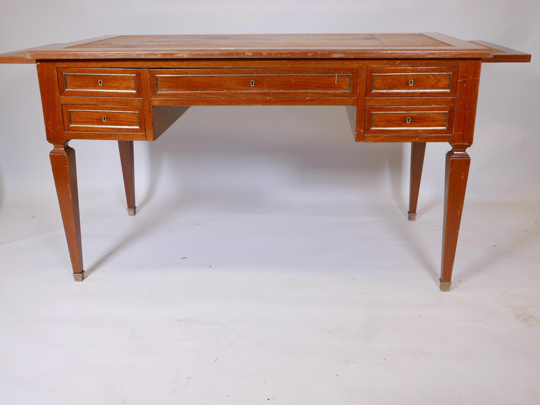 A French mahogany five drawer desk, with brass mouldings, slides to each end, and inset leather top,