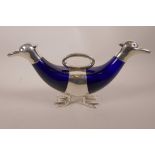 A silver plated and blue glass two section decanter with duck head spouts and duck feet supports,