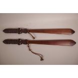 A pair of Maori wooden taiaha staff weapons with carved tribal patterns to the arero (tongue) and