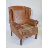 A tan brown leather wing armchair on reeded supports