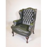 A green leather wing armchair, matches previous lot