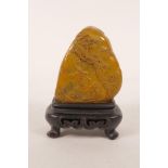 A Chinese carved amber soapstone ornament decorated with figures in a landscape, mounted on a carved
