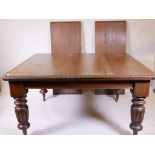 A Victorian oak wind out dining table with two extra leaves, raised on turned and carved supports