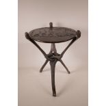 An African hardwood occasional table on a triform folding base, with carved decoration to the top,