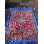 A large deep red ground Persian full pile Mashad carpet, with a floral medallion design, 106" x 142"